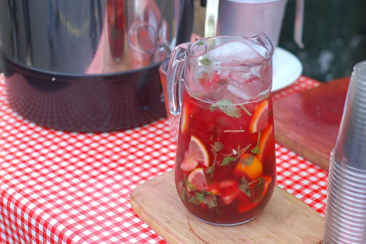A large glass pitcher of sangria with orange and lemon slices on a wooden table